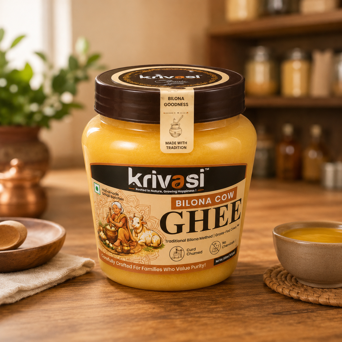 A jar of Krivasi Bilona Cow Ghee placed on a wooden table in a warm kitchen setting, with a small bowl of the yellow ghee, spices, and plants blurred in the background.
